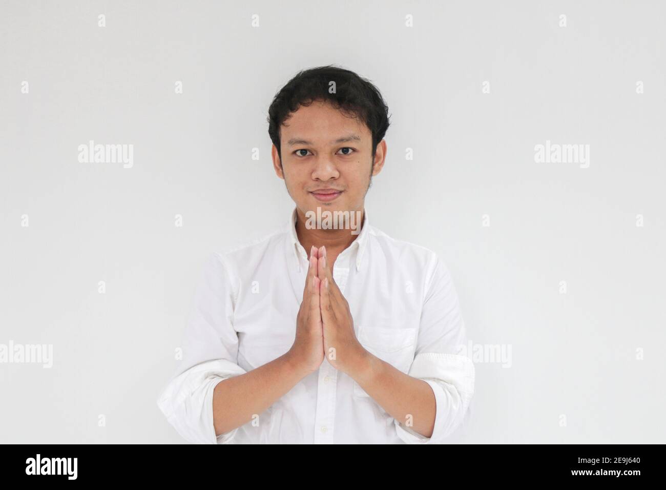 Un jeune homme asiatique portant une chemise blanche donne la main de salutation avec un grand sourire sur son visage. Indonésien sur fond gris. EID Mubarak / Eid Fitr / Banque D'Images