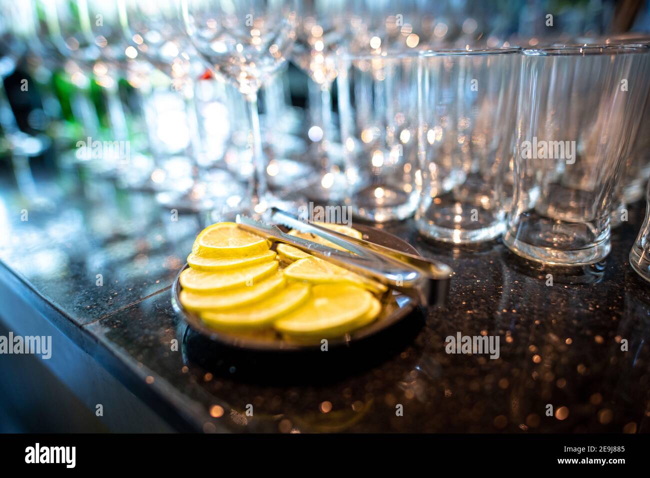 Des tranches de citron dans une assiette noire sont placées sur un comptoir en granit. De nombreux verres d'eau et de vin créent de beaux bokeh, élégant et romantique Banque D'Images