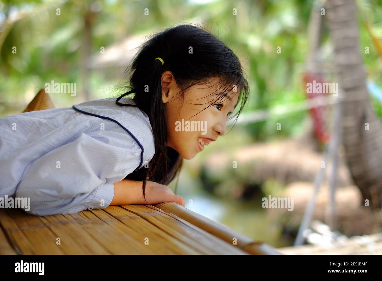 Une jolie jeune fille asiatique penchée sur le bord d'une balustrade, regardant vers le bas, visite, se sentant heureuse et souriante. Banque D'Images