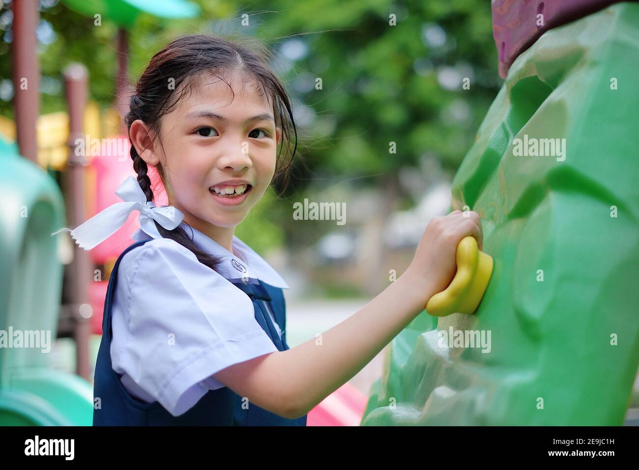 Une adorable jeune fille asiatique en uniforme blanc et bleu d'école joue à l'escalade dans un terrain de jeu, s'entraîner et s'amuser. Banque D'Images