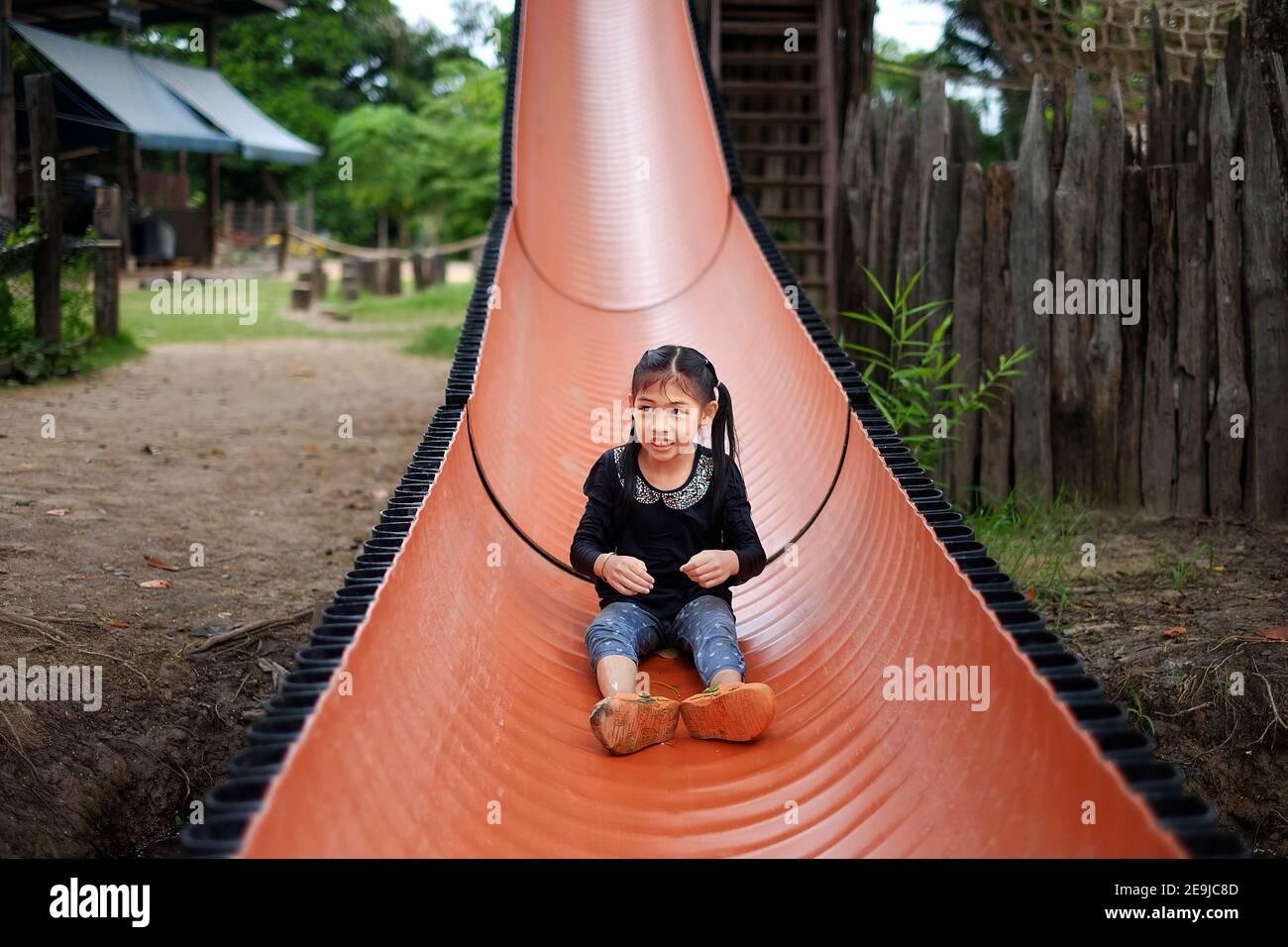 Une jeune fille asiatique mignonne glisser vers le bas d'une longue diapositive orange, s'amusant et souriant. Banque D'Images