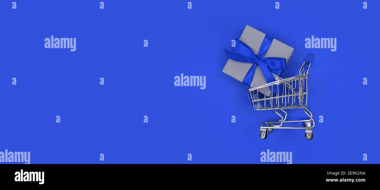 Chariot de supermarché et boîte cadeau sur fond bleu avec espace pour copier. Concept commercial. Banque D'Images