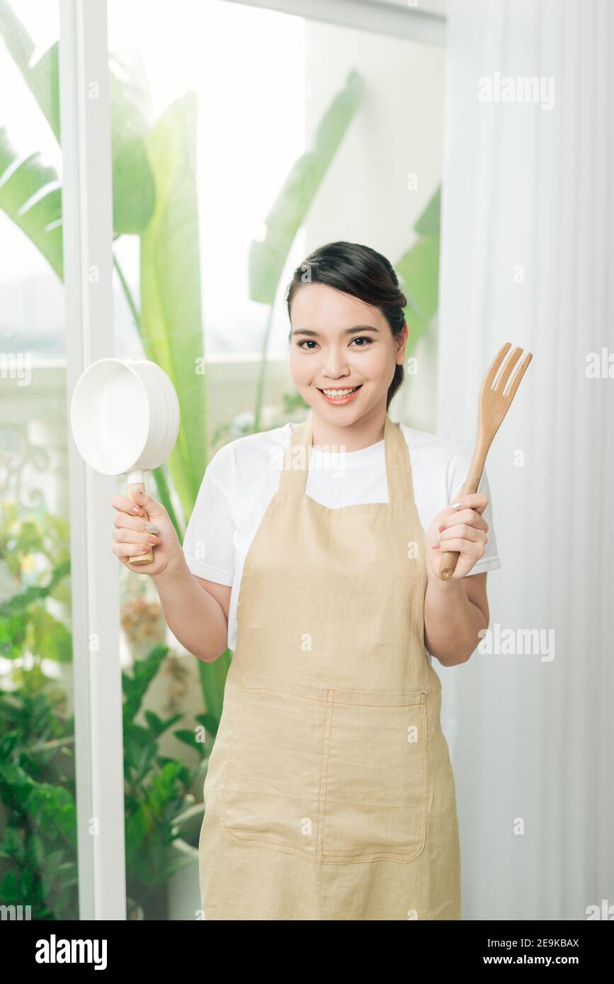 Jeune femme portant un tablier de cuisine avec une poêle Banque D'Images