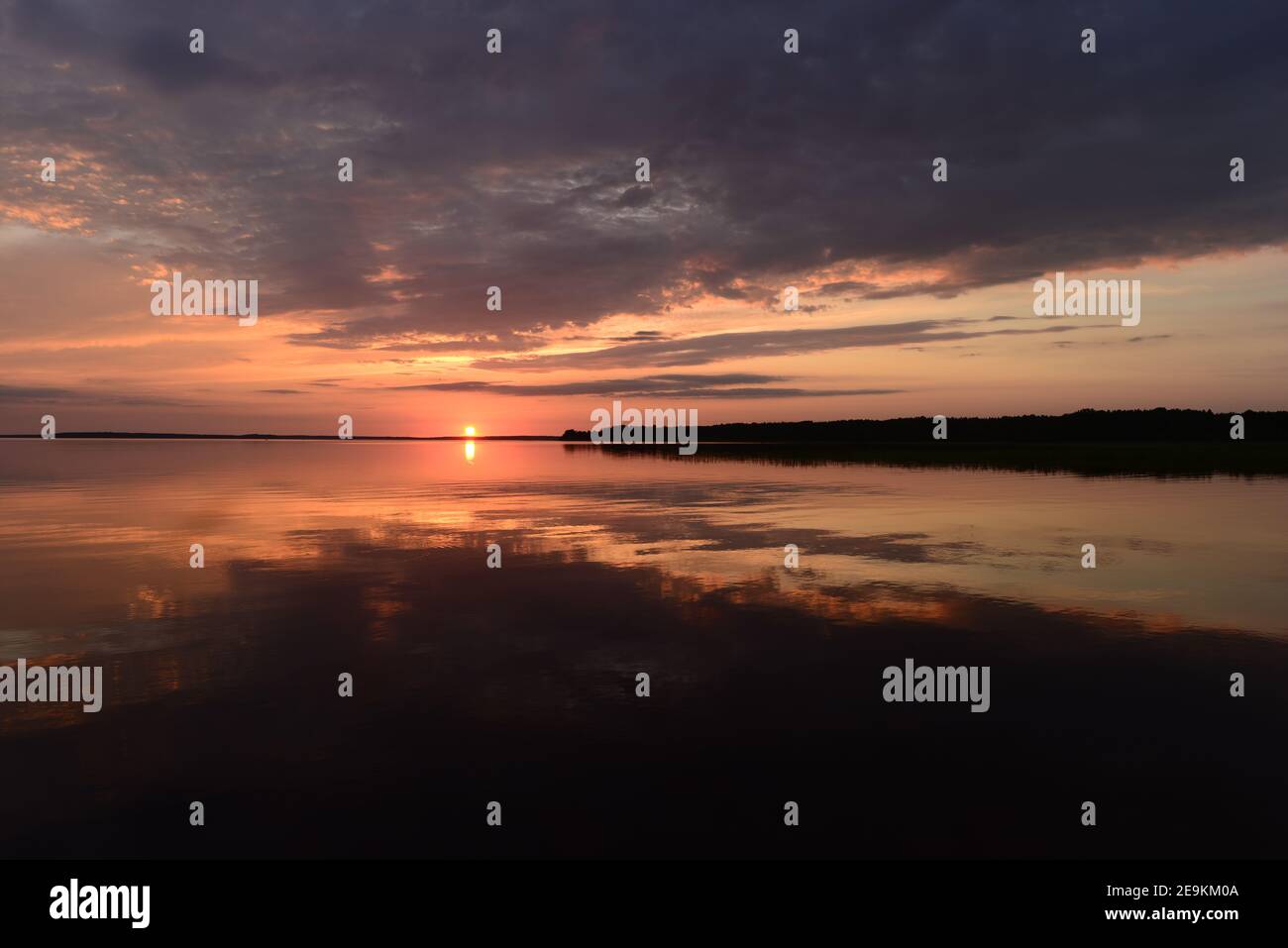 Ciel dans le crépuscule lumineux d'un coucher de soleil lac pittoresque avec nuages réfléchissants et sunbeam sur le horizon sur la surface de l'eau Banque D'Images