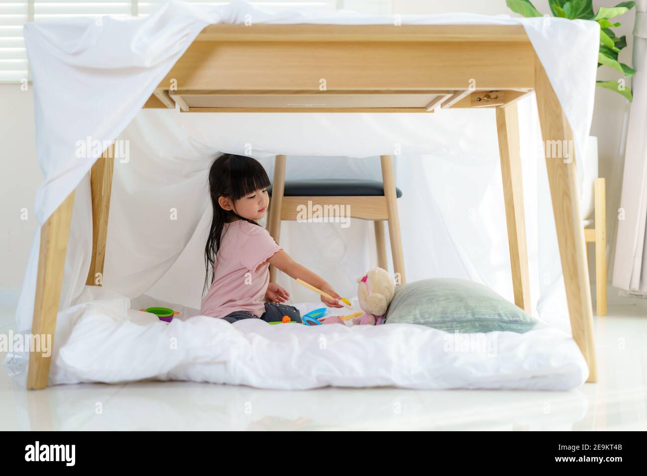 Asiatique mignon petite fille jouer la cuisine et la nourriture à sa poupée tout en étant assise dans une couverture fort dans la vie chambre à la maison pour une escapade parfaite Banque D'Images