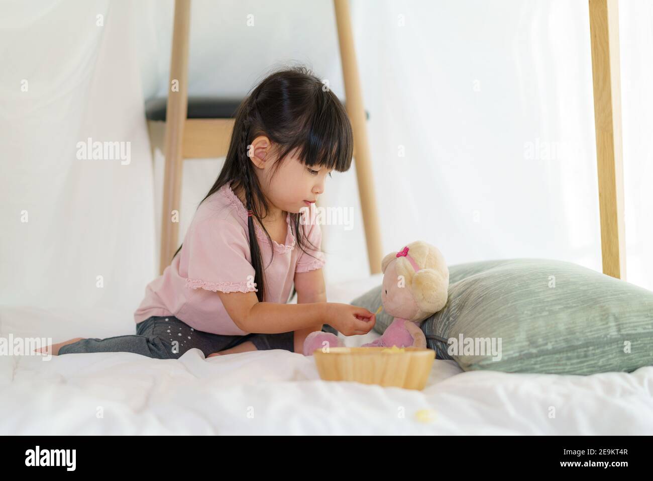 Petite fille asiatique mignonne jouer sa poupée et manger snack tout en étant assis dans une couverture fort dans le salon à la maison pour un refuge parfait loin de leur othe Banque D'Images