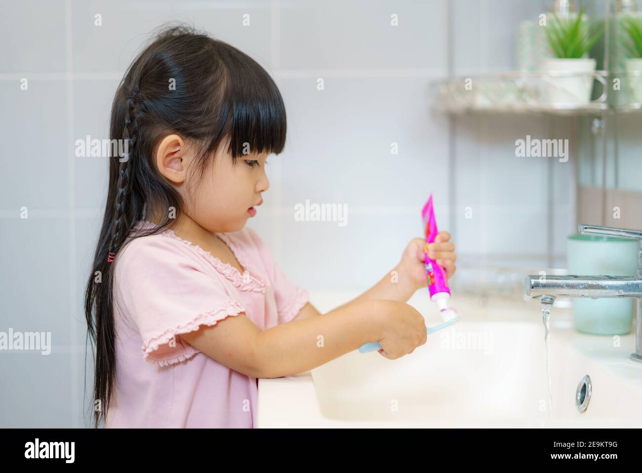 Asiatique mignon enfant fille ou enfant pressez le dentifrice dans la brosse à dents avant de se brosser les dents dans la salle de bains. Hygiène dentaire concept de soins de santé. Banque D'Images