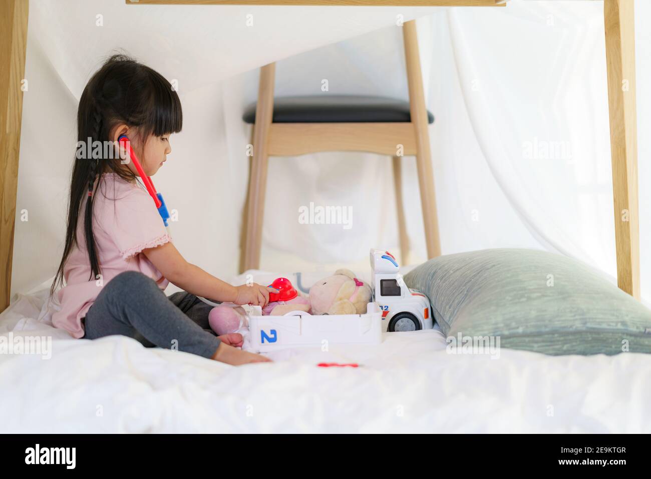Asiatique mignon petite fille jouant docteur modèle de rôle tout en étant assis dans une couverture fort dans la salle de séjour à la maison pour un refuge parfait loin de leur autre famille Banque D'Images