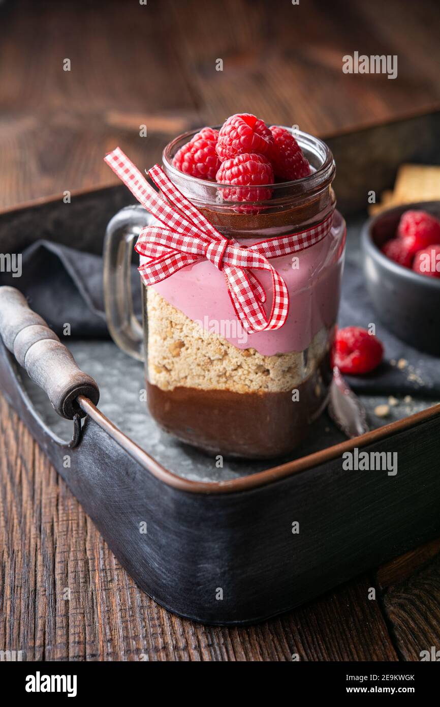 Dessert sans cuisson avec mousse au chocolat noir, biscuits écrasés et fromage à la crème à la framboise dans un pot en verre sur fond de bois rustique Banque D'Images