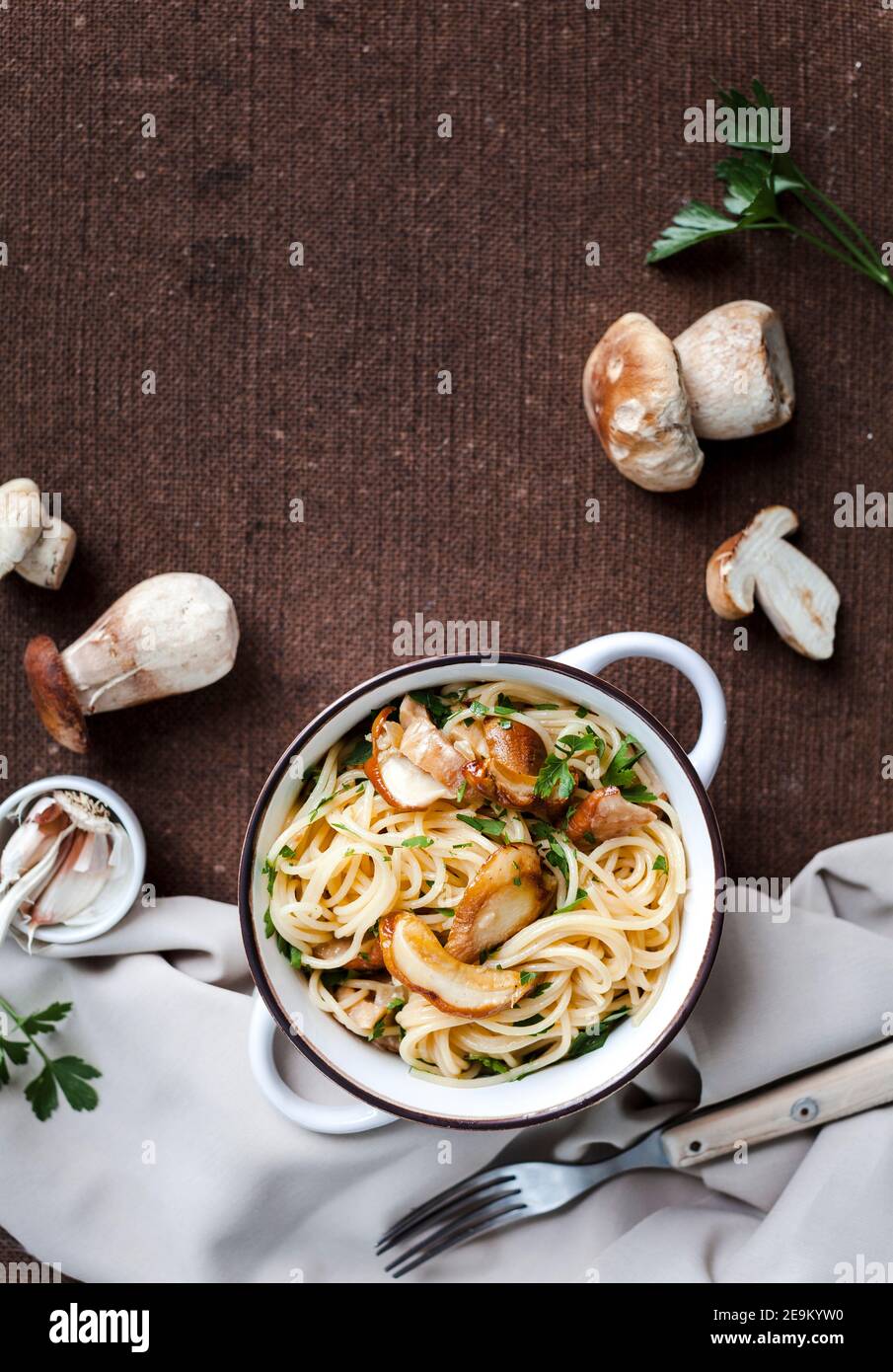 Pâtes avec champignons porcini frais et persil dans un blanc pot vintage sur une nappe brune Banque D'Images