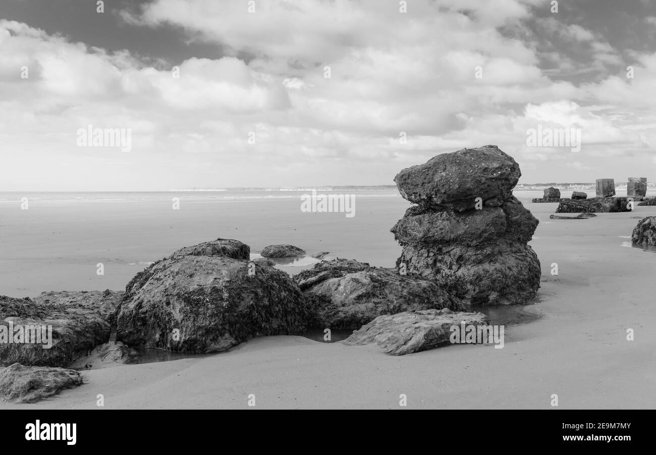 De grands blocs de pierre utilisés comme défenses marines pendant la Seconde Guerre mondiale le long de la plage de sable à marée basse sous un ciel lumineux près de Fraisthorpe, Yorkshire, Royaume-Uni. Banque D'Images