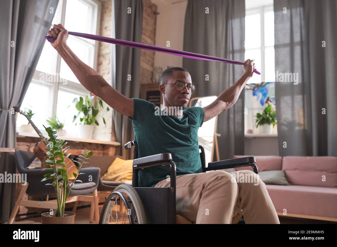 Homme africain handicapé assis en fauteuil roulant levant les bras et faire des exercices d'étirement pendant l'entraînement sportif à la maison Banque D'Images
