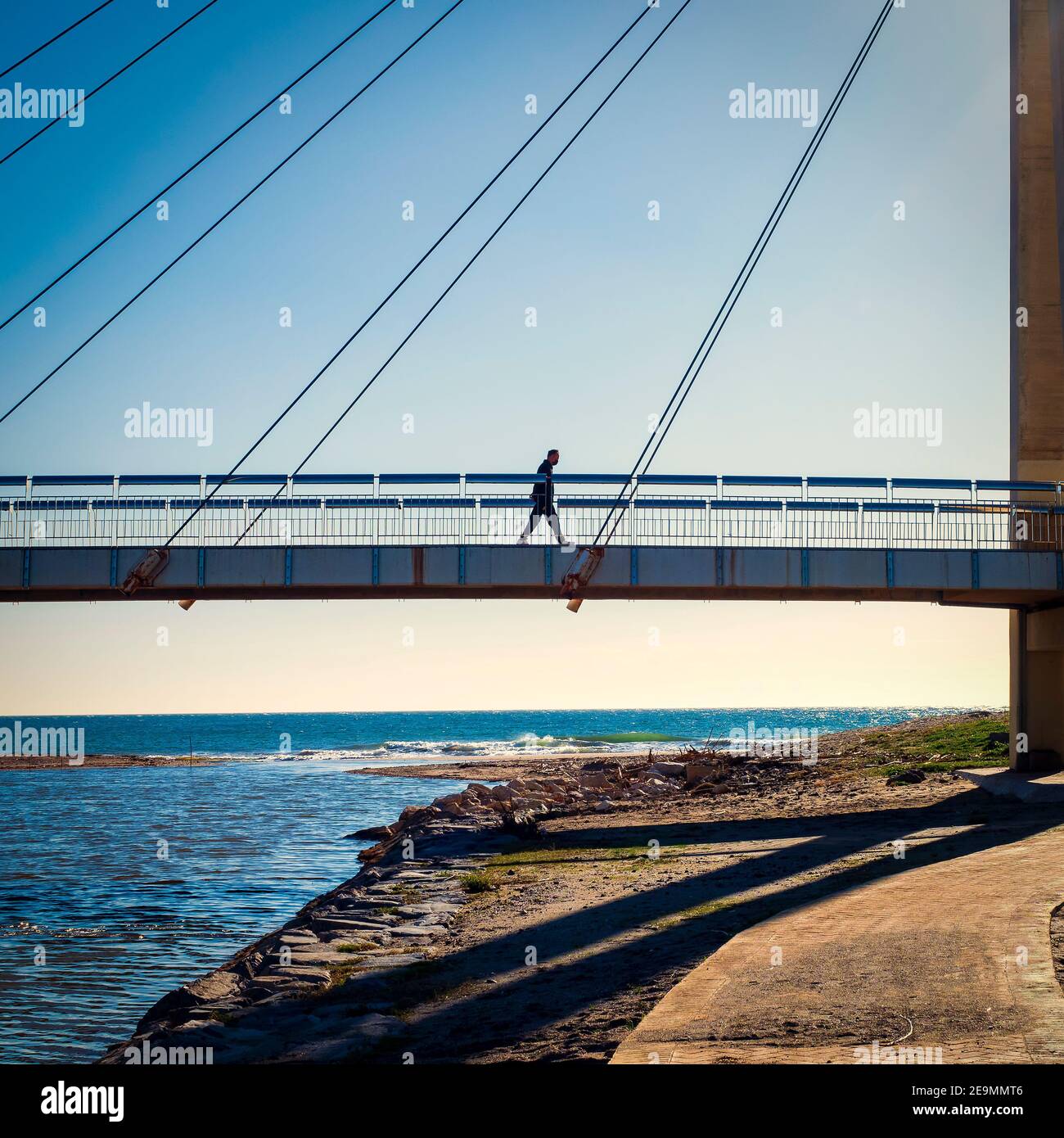Un homme marche à travers un pont suspendu en face de la mer lors d'une journée d'hiver ensoleillée à Fuengirola. Banque D'Images