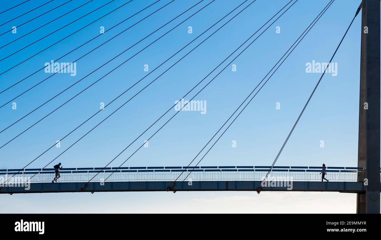 Un homme court dans une femme sur un pont suspendu en face de la mer lors d'une journée d'hiver ensoleillée à Fuengirola. Banque D'Images