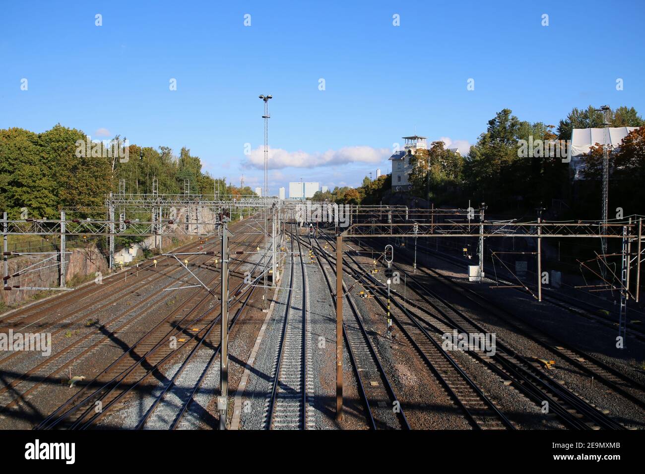 Chemin de fer à Helsinki, Finlande. Photographié sept. 2019. Plusieurs voies de train avec lignes d'alimentation électrique, quelques arbres, ciel bleu et le Mall of Tripla. Banque D'Images