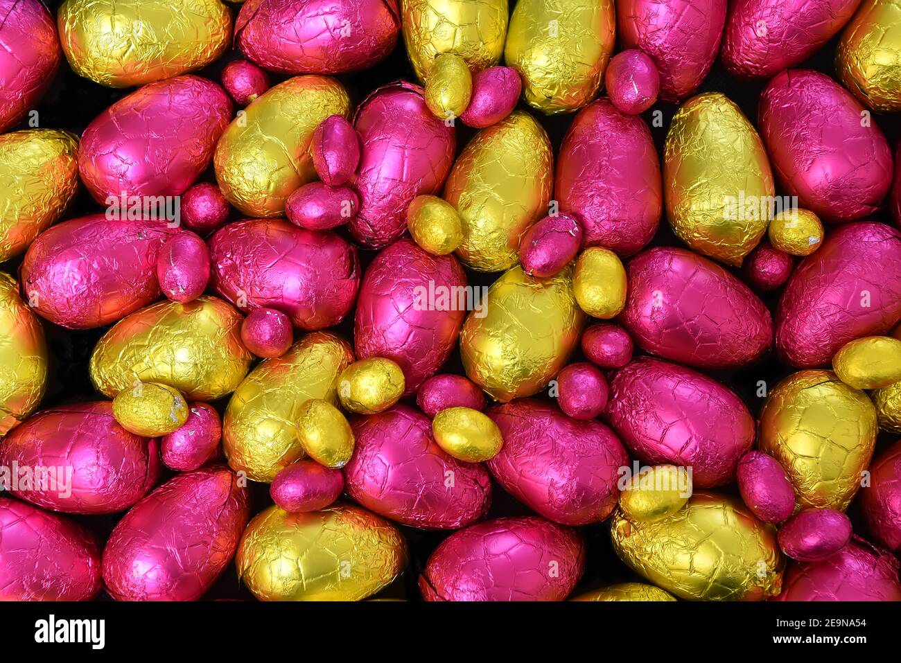 Pile ou groupe de plusieurs couleurs et différentes tailles d'oeufs de pâques au chocolat enveloppés de papier d'aluminium coloré en jaune, or et rose. Banque D'Images