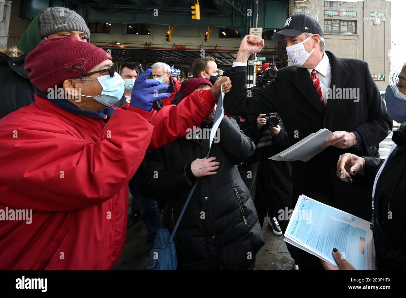 Le maire de New York, Bill de Blasio (cravate rouge), porte une casquette  de baseball des New York Yankees et distribue des dépliants d'information  sur la COVID-19 après une conférence de presse