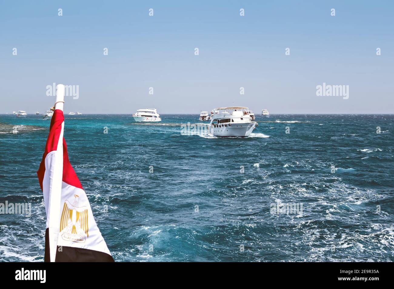Drapeau national de l'Égypte agitant sur le vent de fond bleu ciel. Yachts blancs touristes dans l'eau d'azur Mer Rouge, République arabe d'Egypte. Banque D'Images