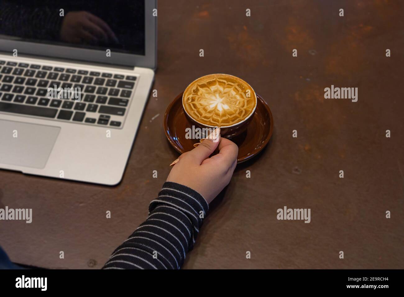 Belle main de femme avec de beaux ongles tenant une tasse de cappuccino à côté d'un ordinateur portable Banque D'Images