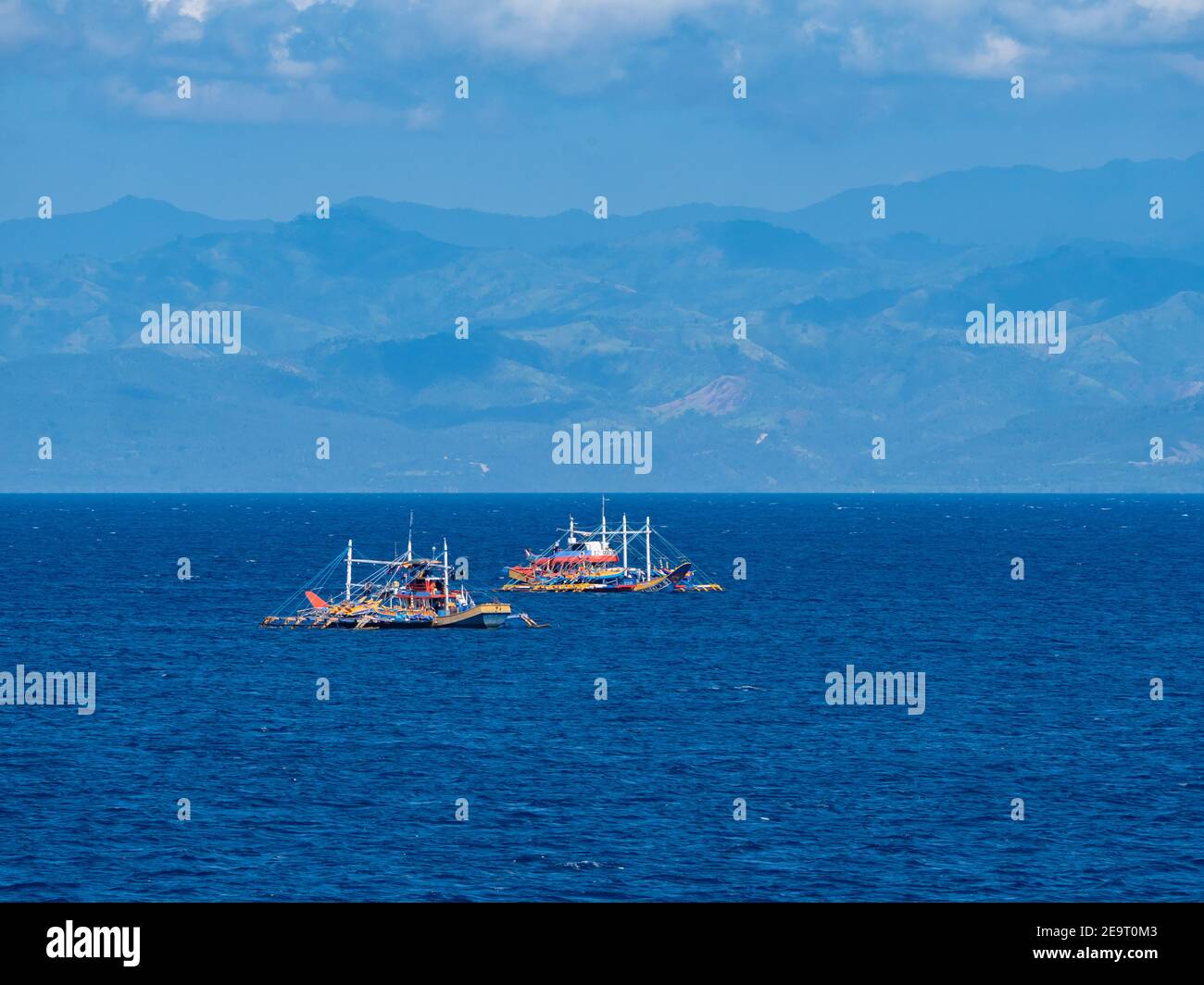 Deux bateaux de pêche traditionnelle au thon en bois avec stabilisateurs à la baie de Sarangani, avec les montagnes de Bayan ng Glan, Sarangani et Davao del sur dans le b Banque D'Images
