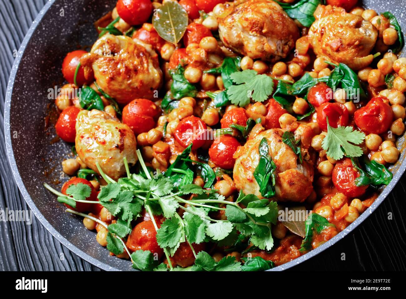 Curry traditionnel de poulet et de pois chiches de cuisses de poulet désossées avec tomates cerises, épinards, gingembre, servi avec de la coriandre fraîche sur une poêle o Banque D'Images