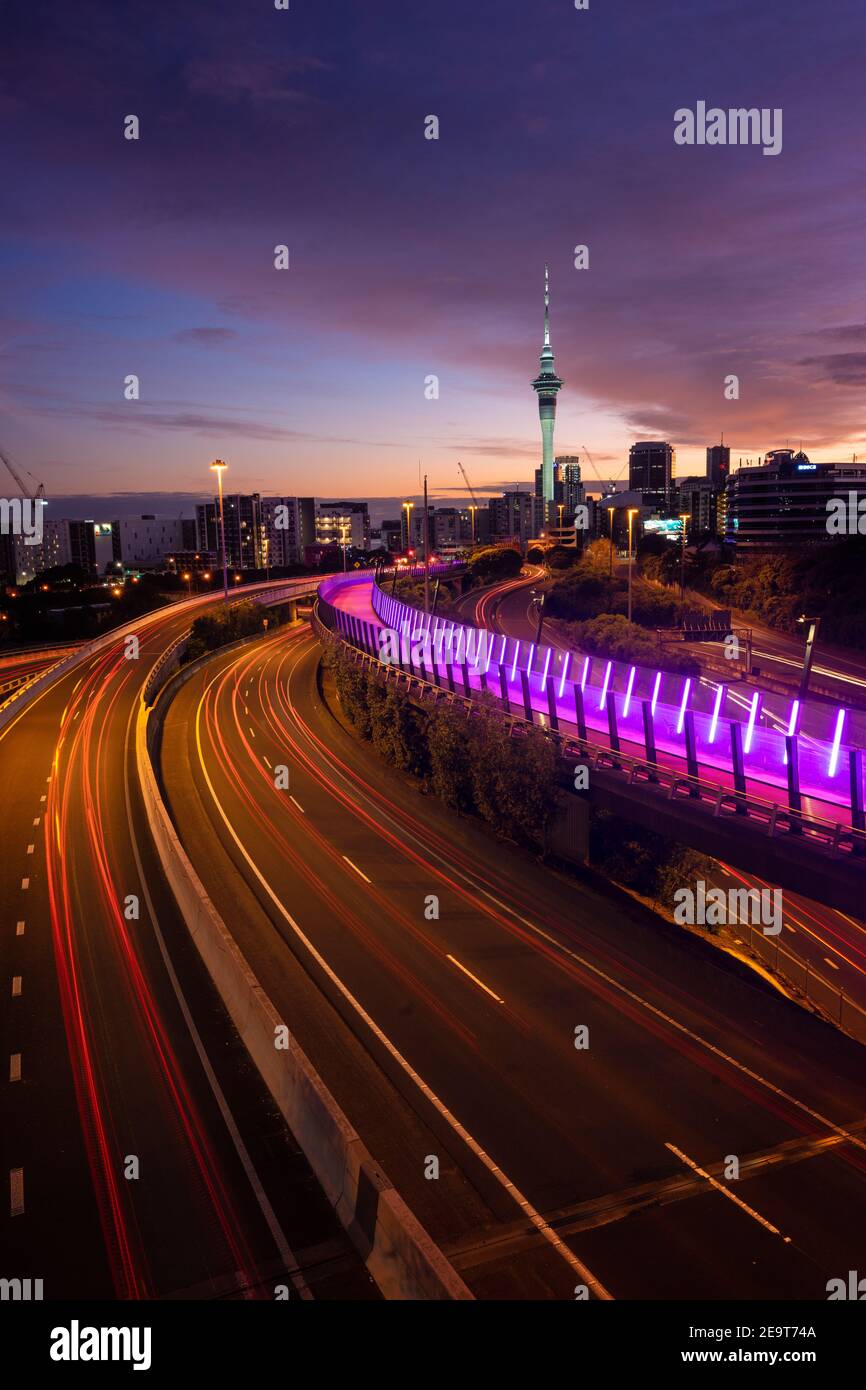 Vue sur la ville d'Auckland, la Sky Tower et l'autoroute avec des pistes de voiture au lever du soleil. Banque D'Images