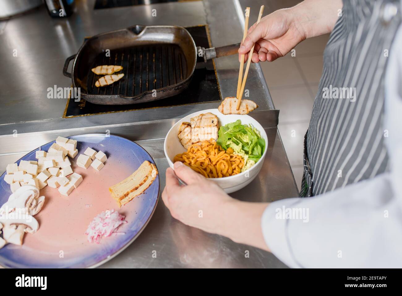 Le filet de poulet frit est placé sur l'assiette. Le chef cuisinier prépare des nouilles spaghetti pour la soupe de ramen. Cuisson de la soupe de ramen avec de la viande, des champignons, du radis et des œufs. Banque D'Images