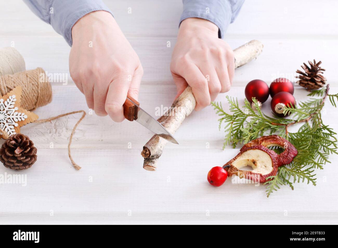 Fleuriste au travail: Femme montre comment faire une décoration de Noël naturelle, en utilisant un bâton de bouleau, des brindilles de thuya, des cônes et des pommes séchées. Étape par étape, tuteur Banque D'Images