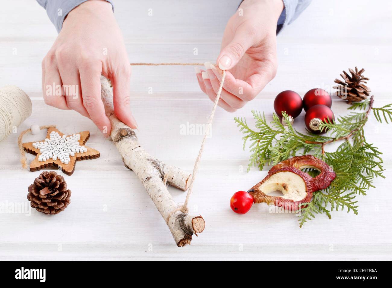 Fleuriste au travail: Femme montre comment faire une décoration de Noël naturelle, en utilisant un bâton de bouleau, des brindilles de thuya, des cônes et des pommes séchées. Étape par étape, tuteur Banque D'Images