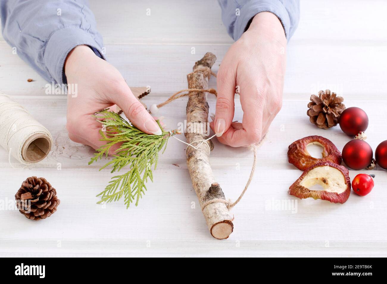 Fleuriste au travail: Femme montre comment faire une décoration de Noël naturelle, en utilisant un bâton de bouleau, des brindilles de thuya, des cônes et des pommes séchées. Étape par étape, tuteur Banque D'Images