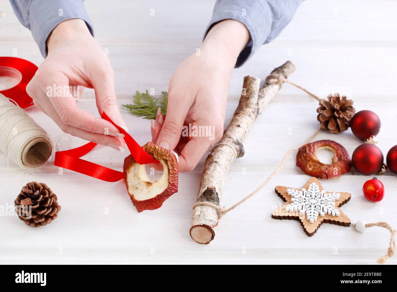 Fleuriste au travail: Femme montre comment faire une décoration de Noël naturelle, en utilisant un bâton de bouleau, des brindilles de thuya, des cônes et des pommes séchées. Étape par étape, tuteur Banque D'Images