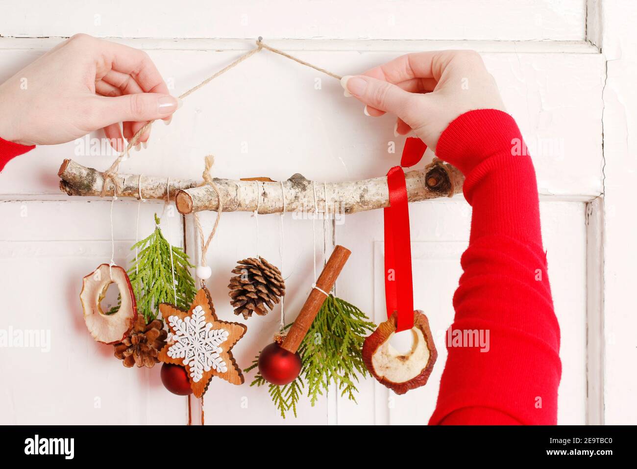Fleuriste au travail: Femme montre comment faire une décoration de Noël naturelle, en utilisant un bâton de bouleau, des brindilles de thuya, des cônes et des pommes séchées. Étape par étape, tuteur Banque D'Images