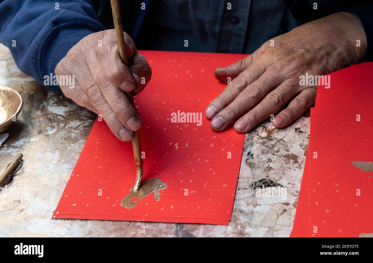 Hong Kong, Hong Kong, Chine. 6 février 2021. Une calligraphie sifu (maître) travaille sur le côté d'une route très fréquentée à Causeway Bay Hong Kong, produisant des couplets cantonais peints à la main prêts pour le nouvel an chinois. Il peint les personnages de Gong hei FAT choy (qui vous souhaite la prospérité!), une expression populaire du nouvel an. Ces couplets lunaires rouges du nouvel an ou cheun lyun, sont utilisés comme décoration et ont beaucoup de différents messages favorables écrits sur eux. CNY commencera le vendredi 12 février 2021 avec les vacances annonçant l'année du zodiaque de l'Ox. Crédit : Jayne Russell/ZUMA Wire/Alay Live News Banque D'Images