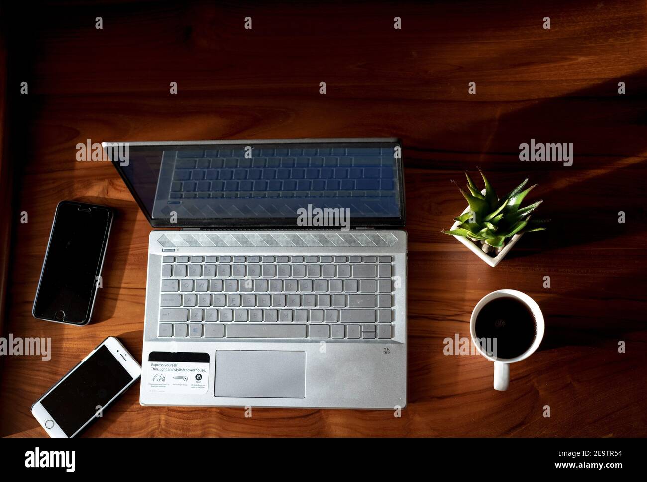 Travailler à la maison avec un ordinateur portable et des téléphones avec un chaud tasse de café à côté et une plante verte Banque D'Images