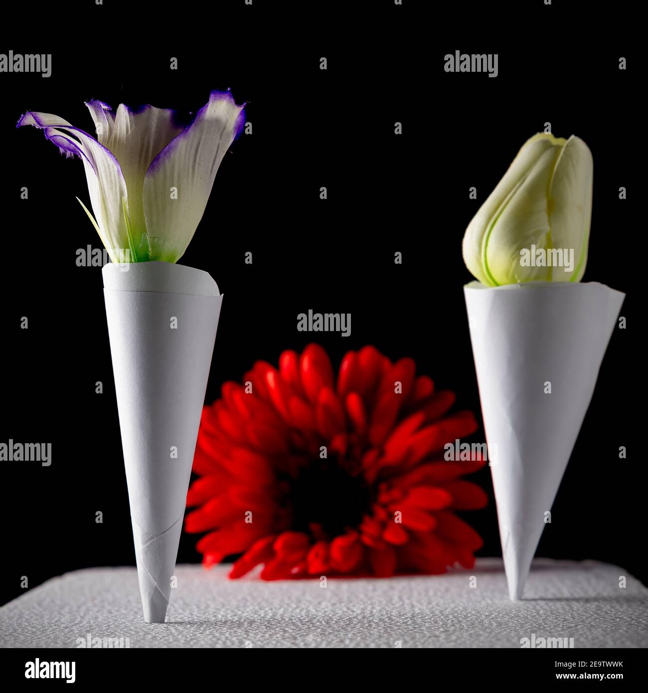 Deux cônes en papier avec fleurs à l'intérieur et une fleur rouge en arrière-plan Banque D'Images
