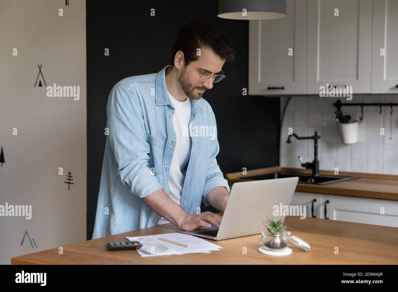 Les jeunes hommes confiants fournissent des paiements en ligne à l'aide d'un ordinateur portable dans la cuisine Banque D'Images