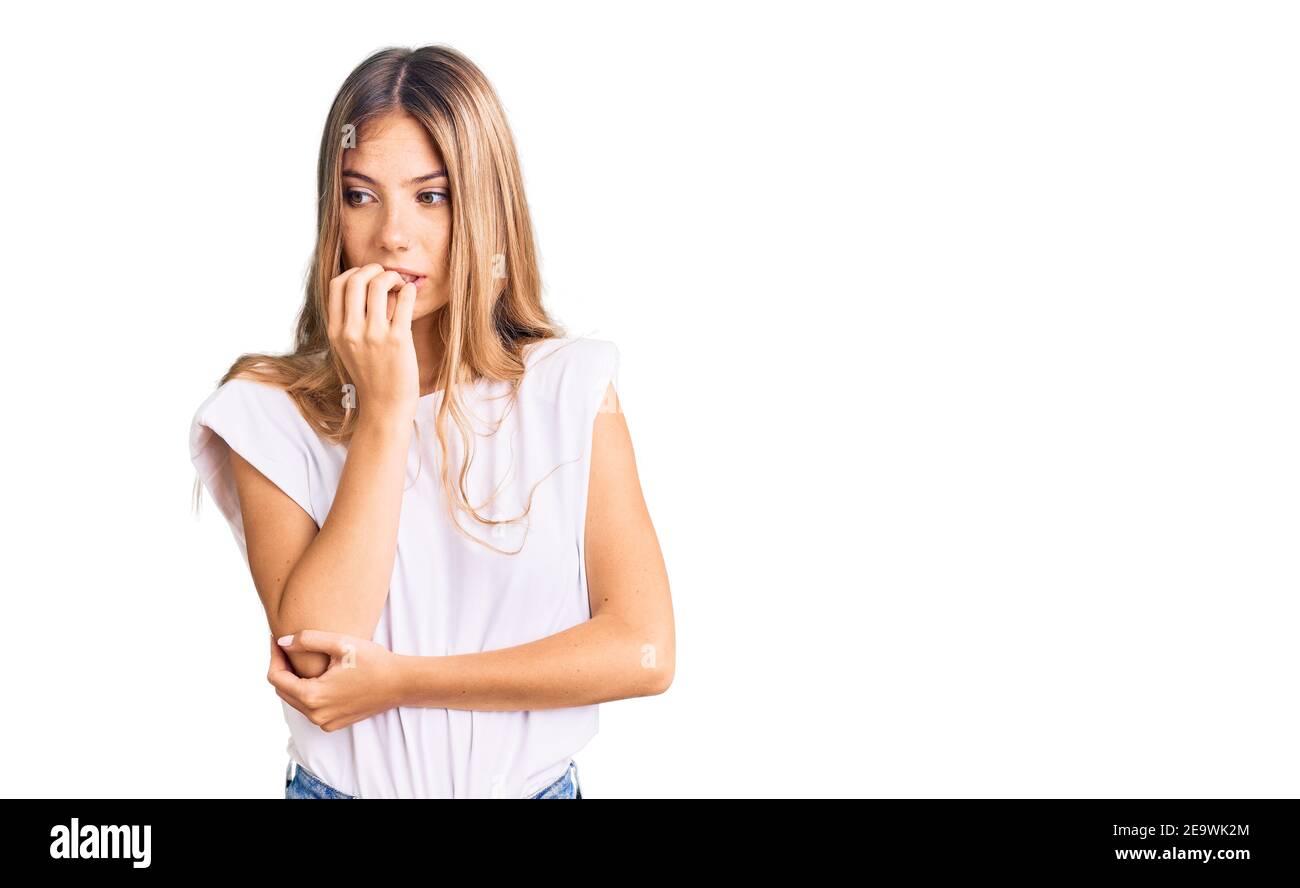 Belle femme caucasienne avec des cheveux blonds portant une chemise blanche et décontractée qui a l'air stressée et nerveuse avec les mains sur la bouche mordant les ongles. Problème d'anxiété. Banque D'Images
