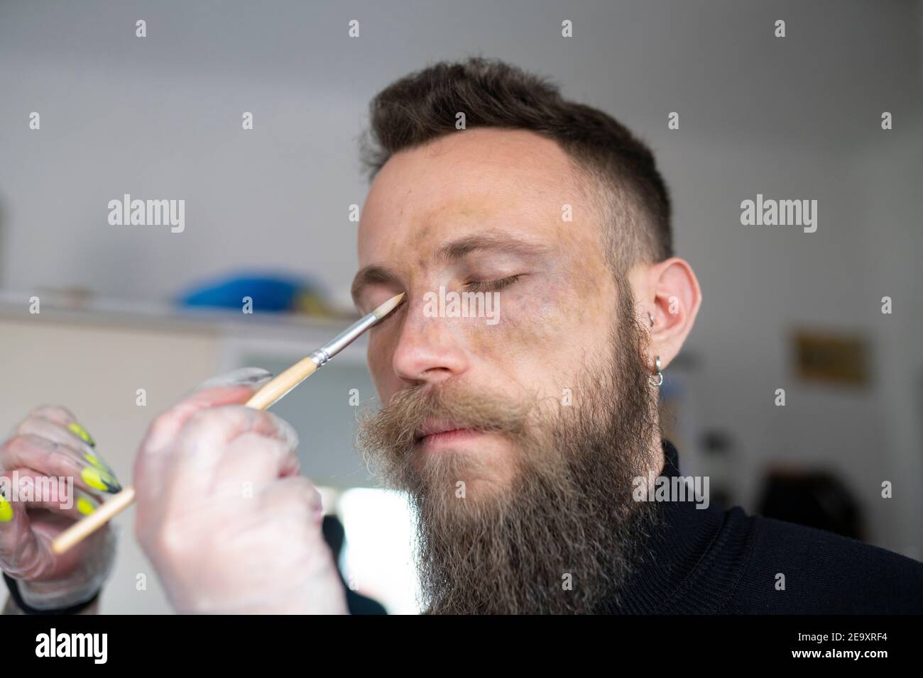 Gros plan d'un maquilleur méconnaissable qui met du maquillage sur un taille basse visage de l'homme Banque D'Images