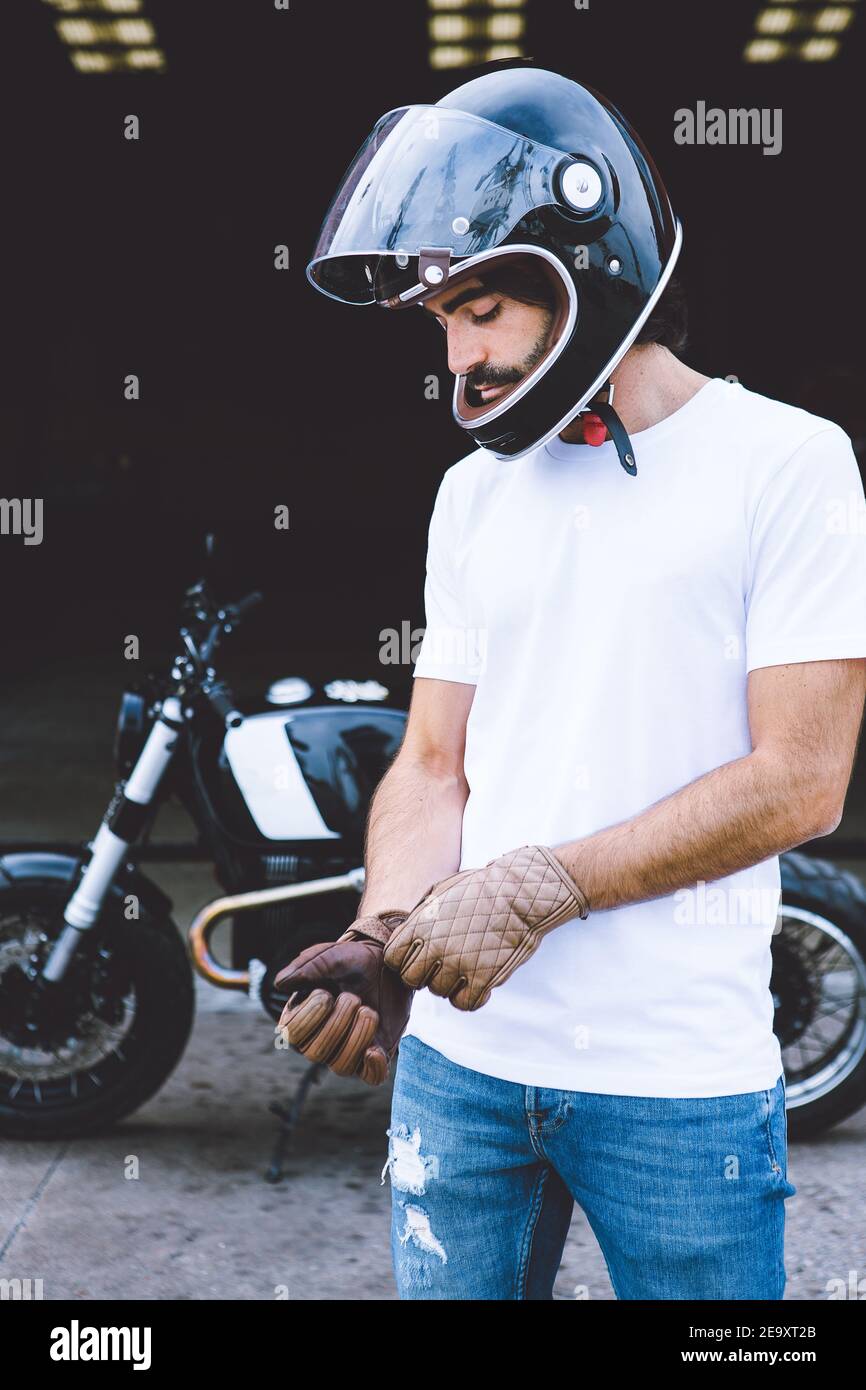 Motard masculin non rasé concentré jeune dans une tenue décontractée et  casque portant des gants en se tenant près de la moto dans la rue Photo  Stock - Alamy
