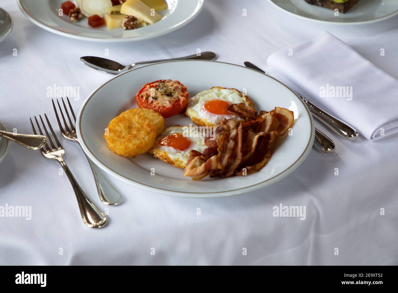 Grand angle d'œufs frits appétissants avec tranches de bacon servies sur l'assiette avec la tomate farcie et la mozzarella croustillante et placé sur la barre de coupe avec cutler et cu Banque D'Images
