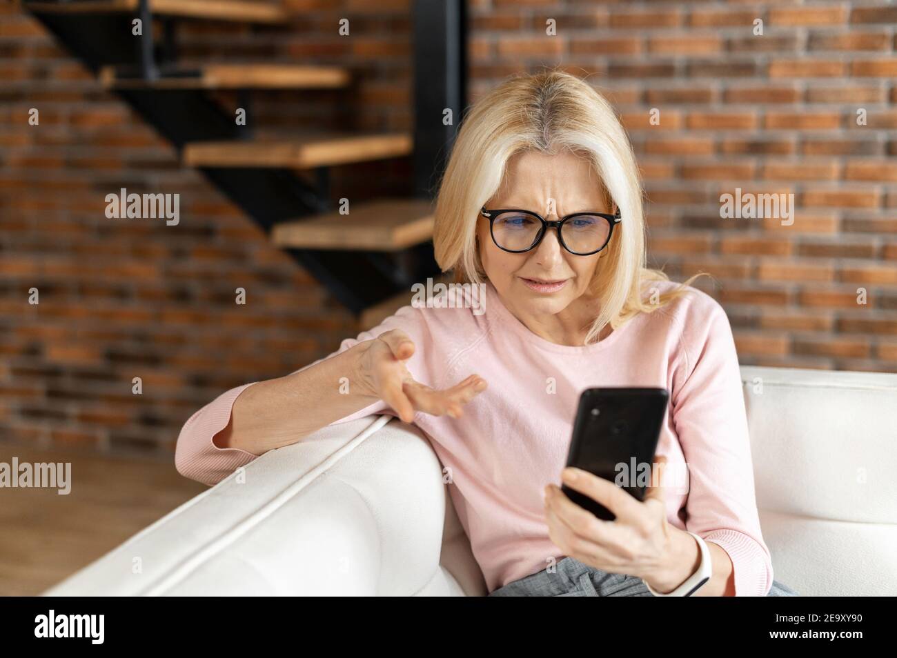 Une femme d'âge moyen perplexe a regardé l'écran d'un smartphone, a mal compris ce qui se passe, a reçu un e-mail désagréable ou a vu de mauvaises nouvelles dans les réseaux Banque D'Images