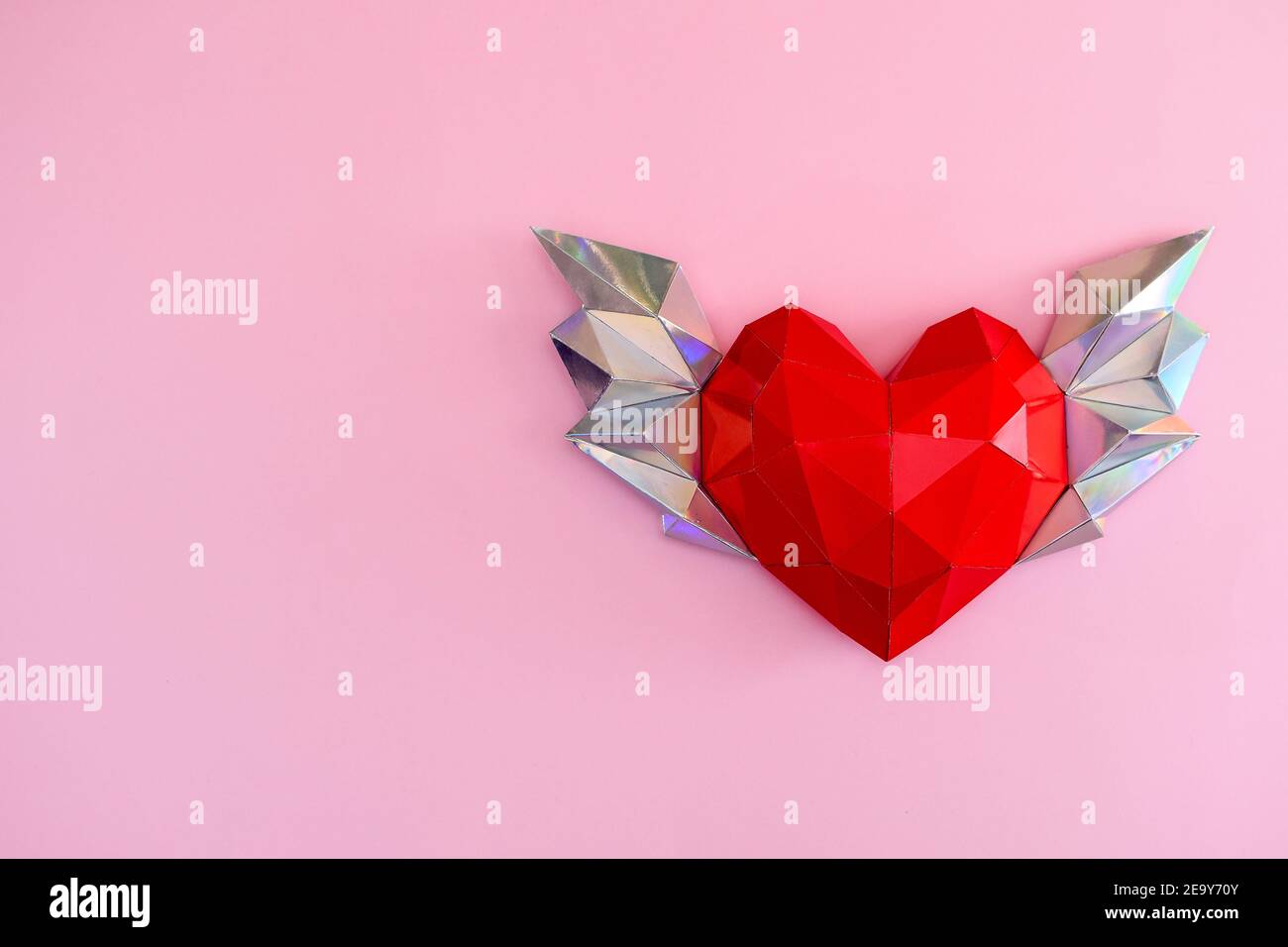 Coeur polygonal avec ailes sur fond rose avec fleurs de coton, boîte cadeau et petits coeurs. Banque D'Images