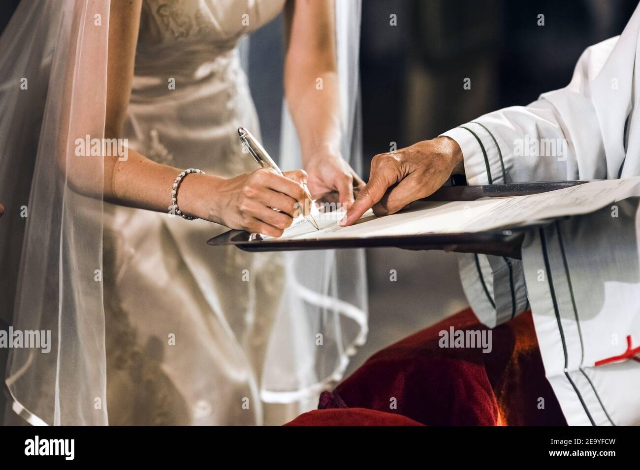 Une mariée signe son contrat de mariage sur l'autel d'une église avec un prêtre. Banque D'Images