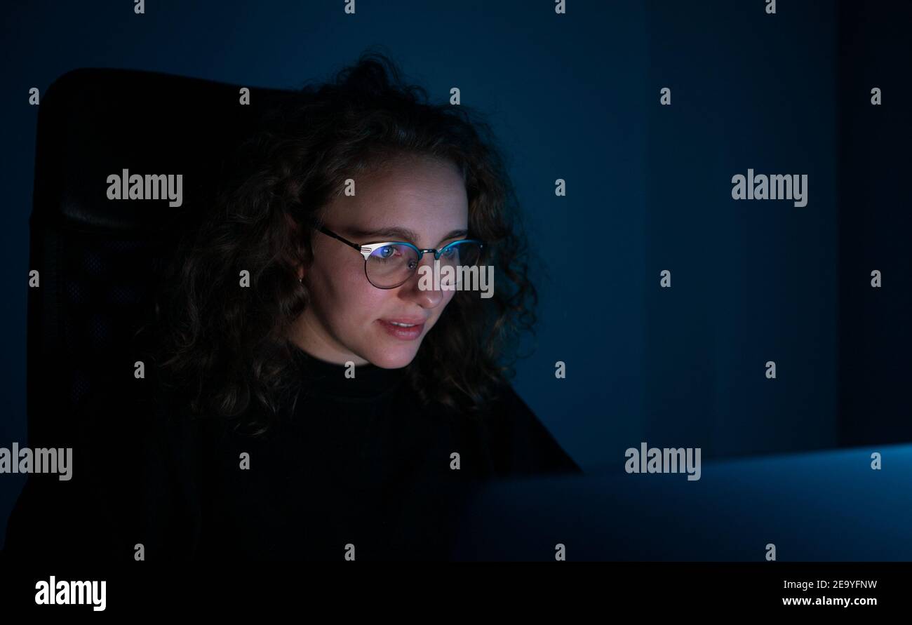 Femme étudiant avec son ordinateur la nuit. Il est sombre et il y a de la lumière bleue. Concept de surcharge de travail. Banque D'Images