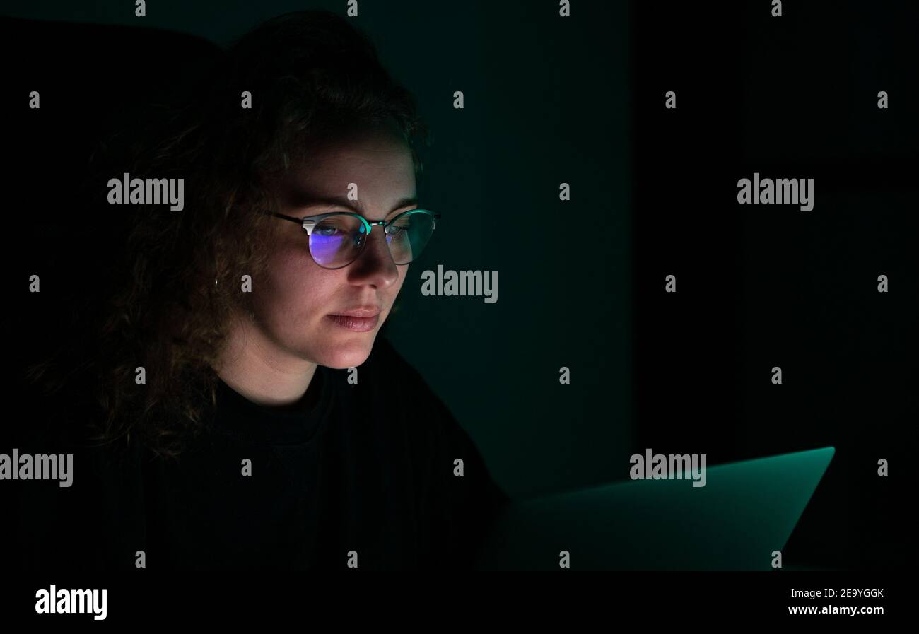 Femme d'affaires aux cheveux bouclés travaillant la nuit avec son ordinateur. Il est sombre et la lumière ambiante est verte. Banque D'Images