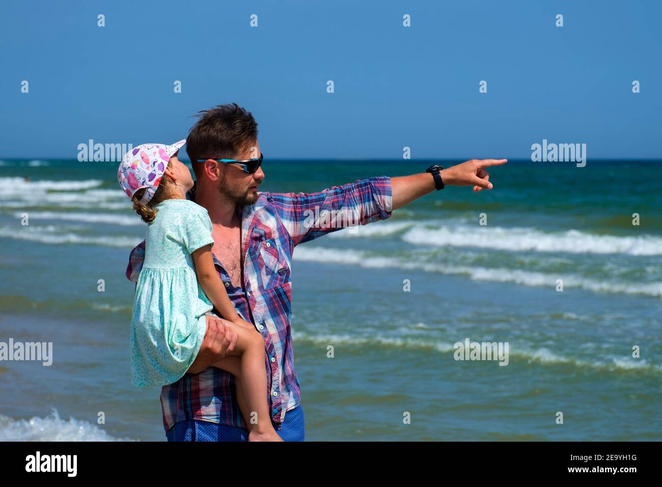 Papa tient sa fille dans ses bras et montre quelque chose loin dans la mer Banque D'Images