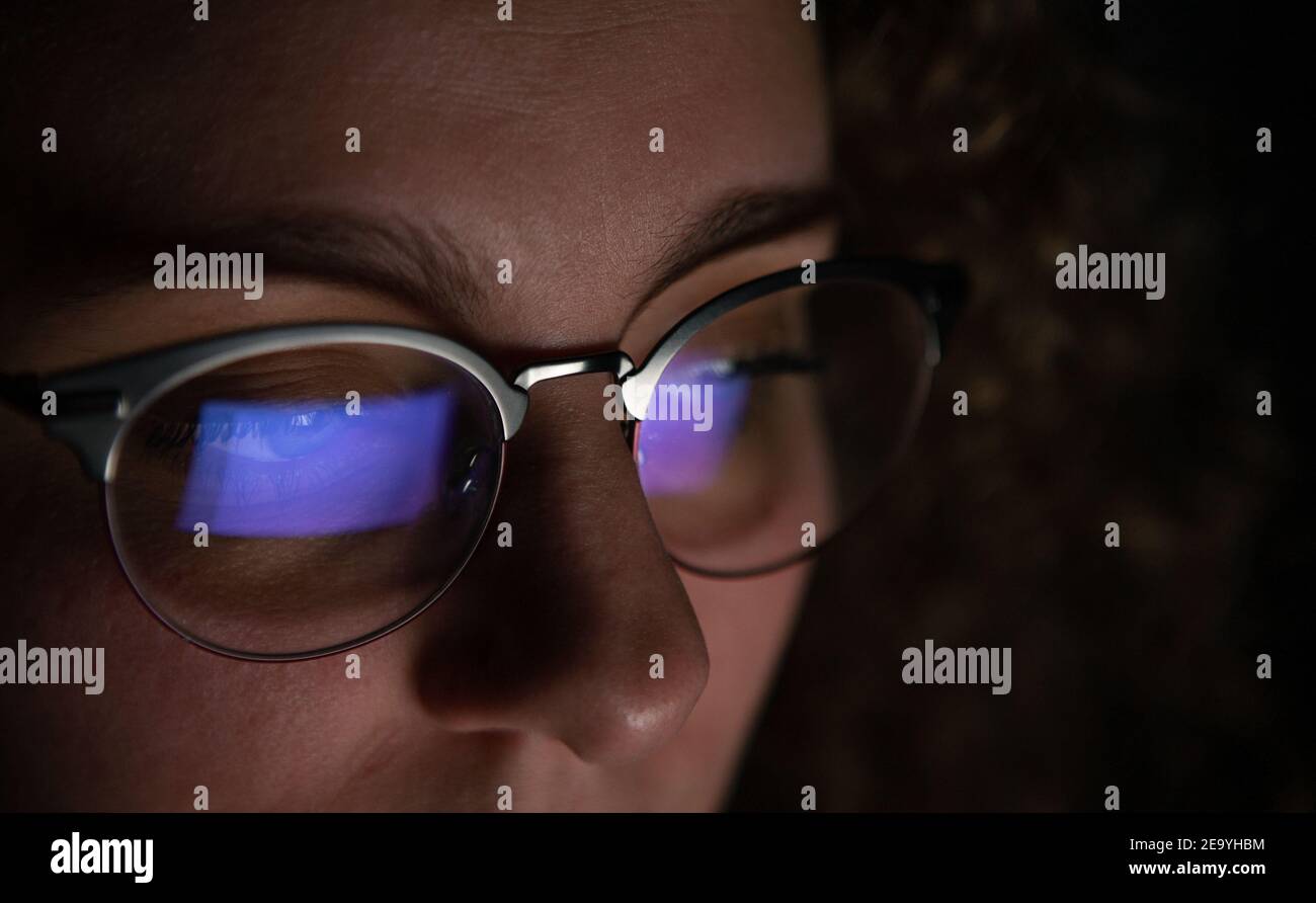 Écran d'ordinateur reflété dans les lunettes d'une femme qui travaille la nuit. Banque D'Images