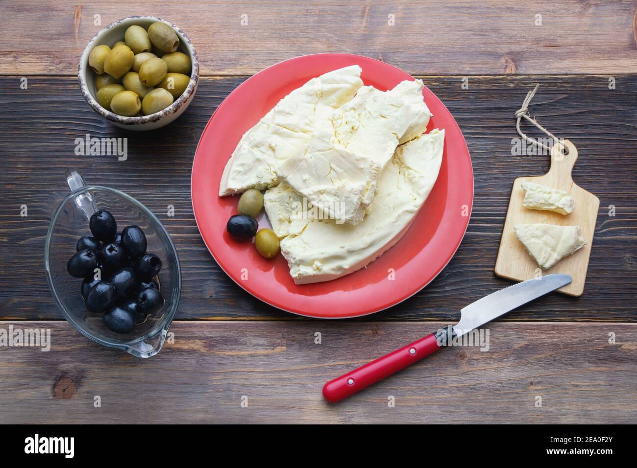 Cuisine des Balkans. Monténégro. Le fromage Pljevaljski est un fromage blanc doux local dans une assiette rouge sur une table rustique sombre Banque D'Images
