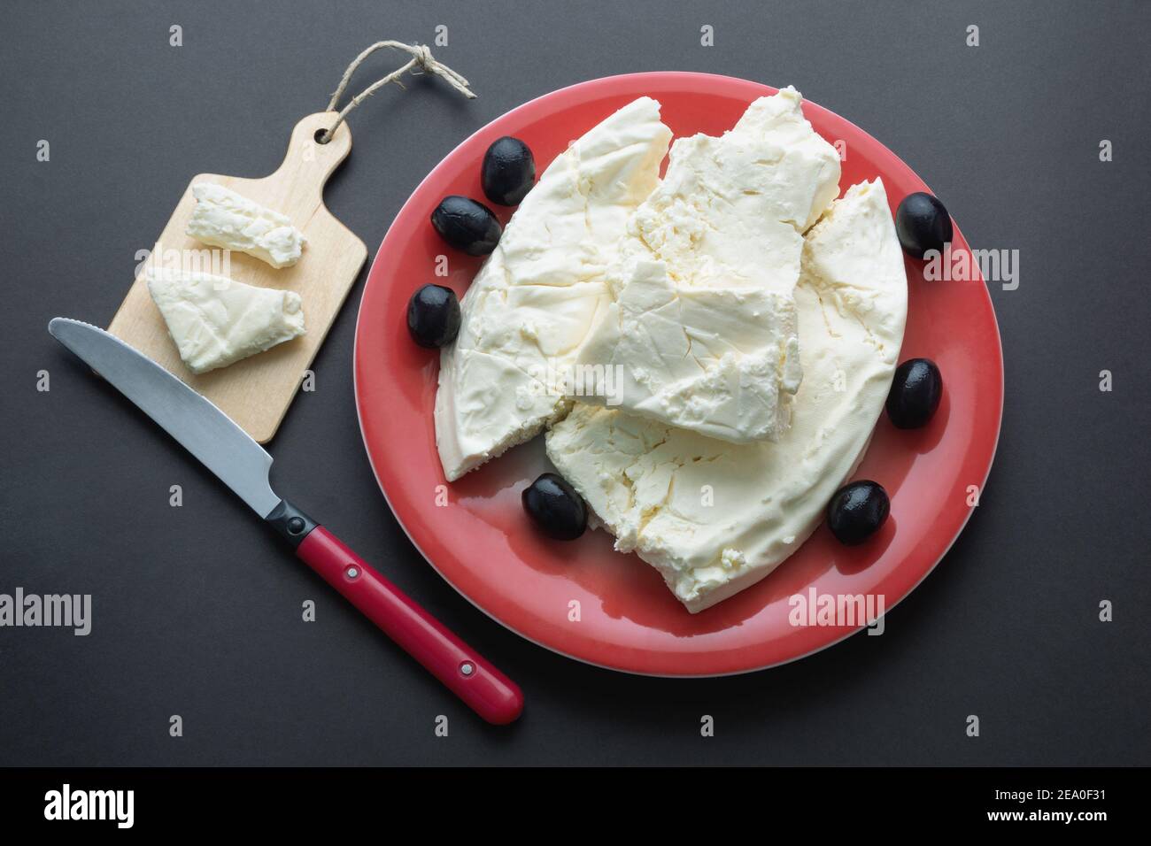 Cuisine des Balkans. Monténégro. Le fromage Pljevaljski est un fromage blanc doux local dans une assiette rouge sur une table rustique sombre Banque D'Images