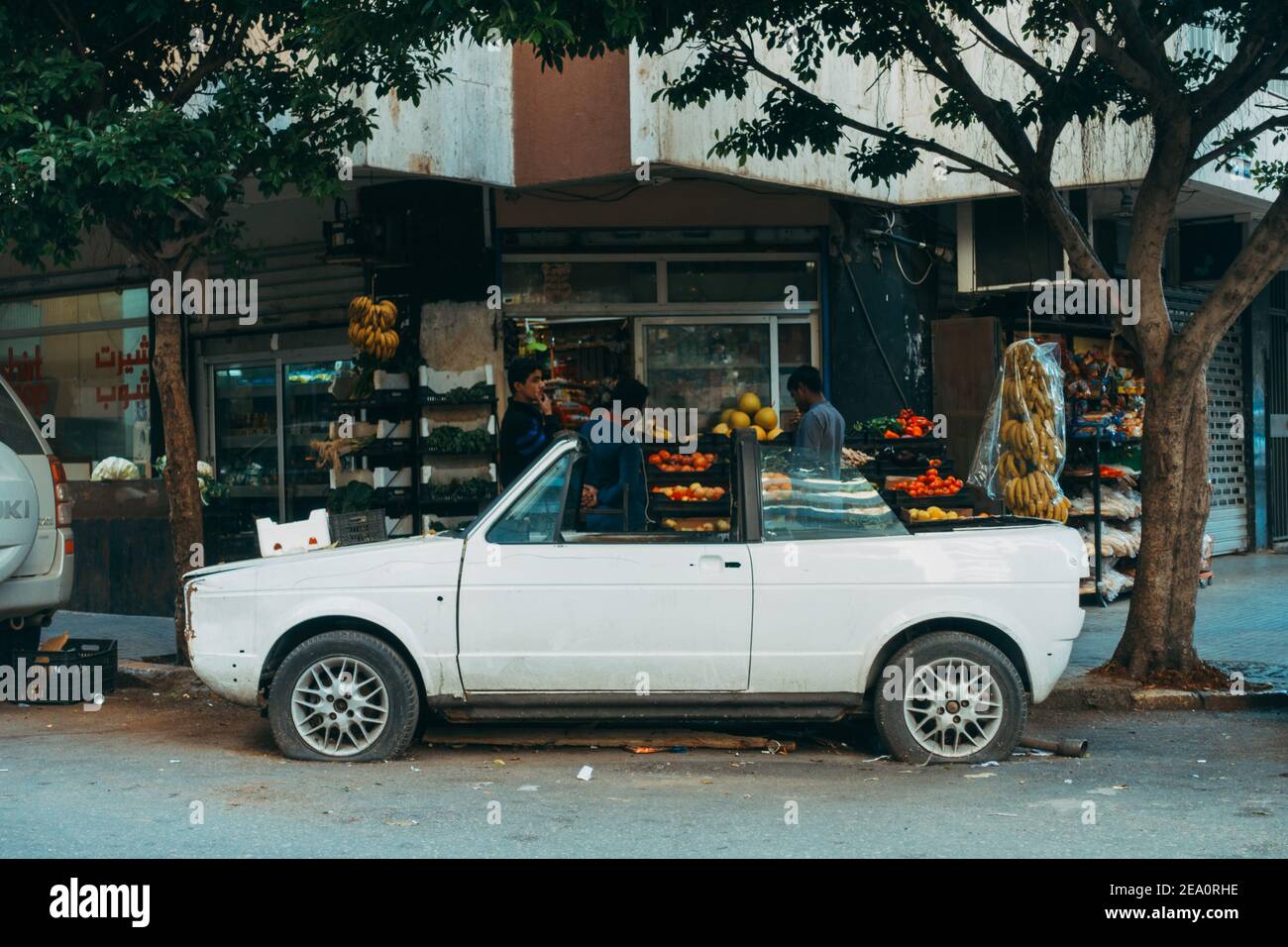 Une voiture décapotable compacte abandonnée avec des pneus dégonflés dans un coin de rue devant un épicier à Beyrouth, au Liban Banque D'Images